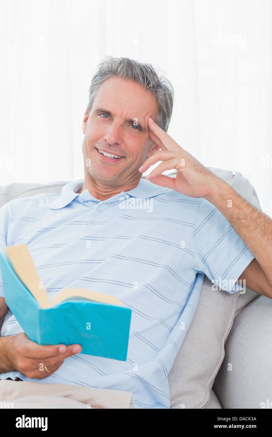 L'homme se détendre sur son lit avec un livre smiling at camera Banque D'Images