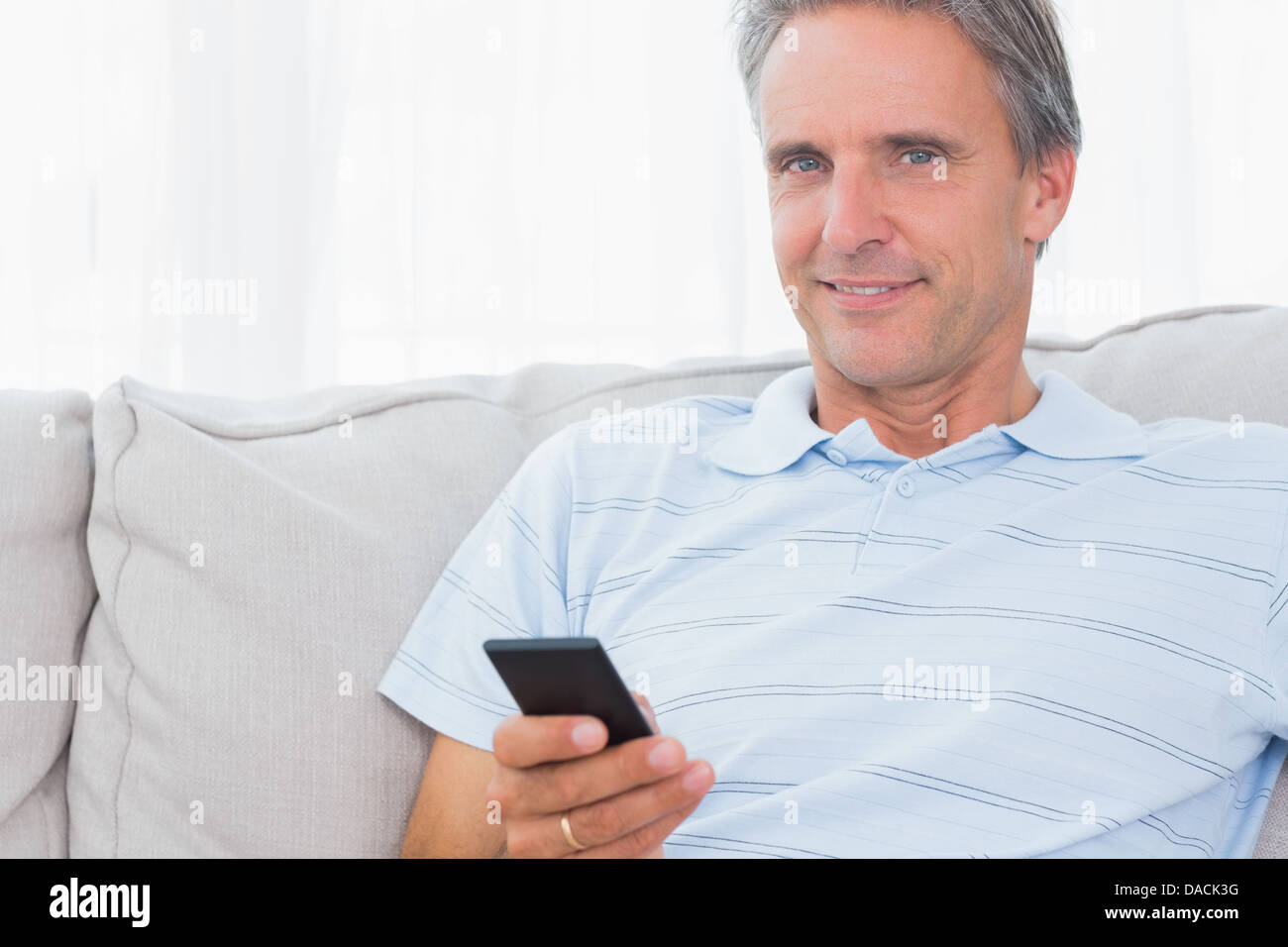 L'homme se détendre sur son canapé l'envoi d'un texte smiling at camera Banque D'Images