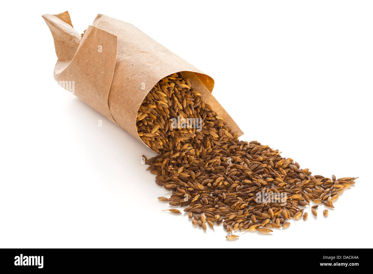 Les graines de cumin grillées déversant de torsion de papier brun, sur fond blanc avec l'ombre doux et naturels, l'avant à l'arrière l'accent Banque D'Images