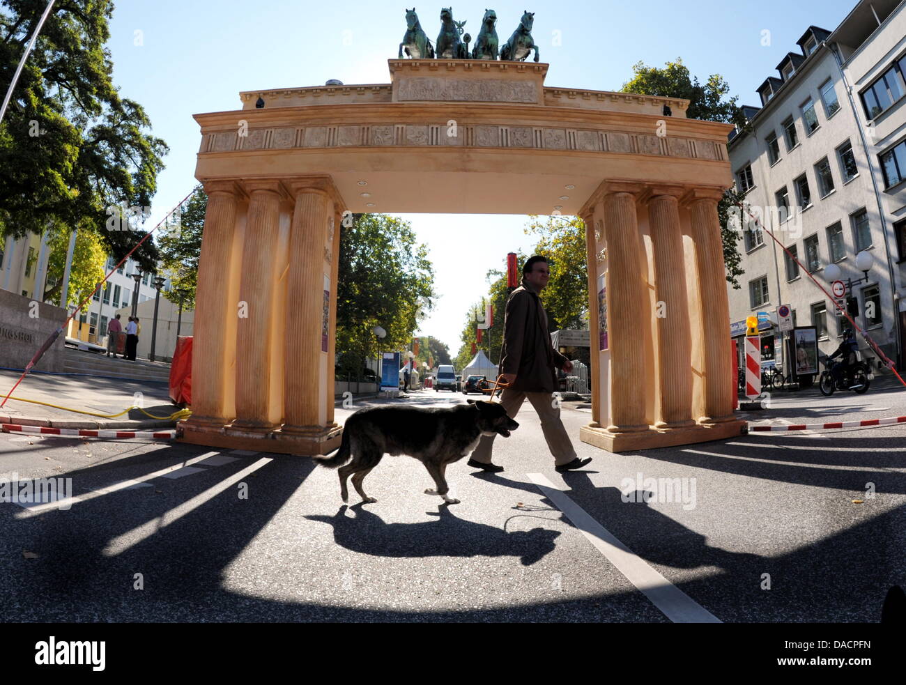 Un homme avec un chien passe devant un modèle de la porte de Brandebourg à Bonn, Allemagne, 30 septembre 2011. Bonn célèbre le Jour de la réunification allemande, le même jour que le jour de la Westphalie. La célébration se passe sur trois jours du 1 au 3 octobre 2011. A trois kilomètres de long street party a été construit et le Président allemand invite les enfants d'une partie à la Villa Hammerschmidt. Photo Banque D'Images