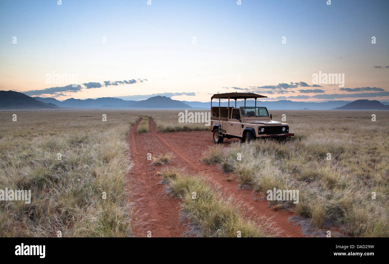 Jeu land rover véhicule stationné par chemin de sable au lever du soleil, Namib Rand game reserve, Namib Naukluft Park, Namibie, Afrique Banque D'Images