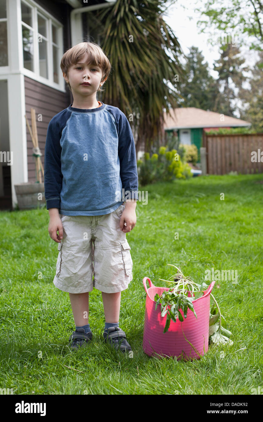 Boy standing in jardin près de refuser de jardinage Banque D'Images