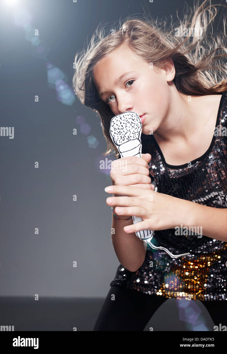 Girl en chantant dans le microphone contre l'arrière-plan gris papier Banque D'Images