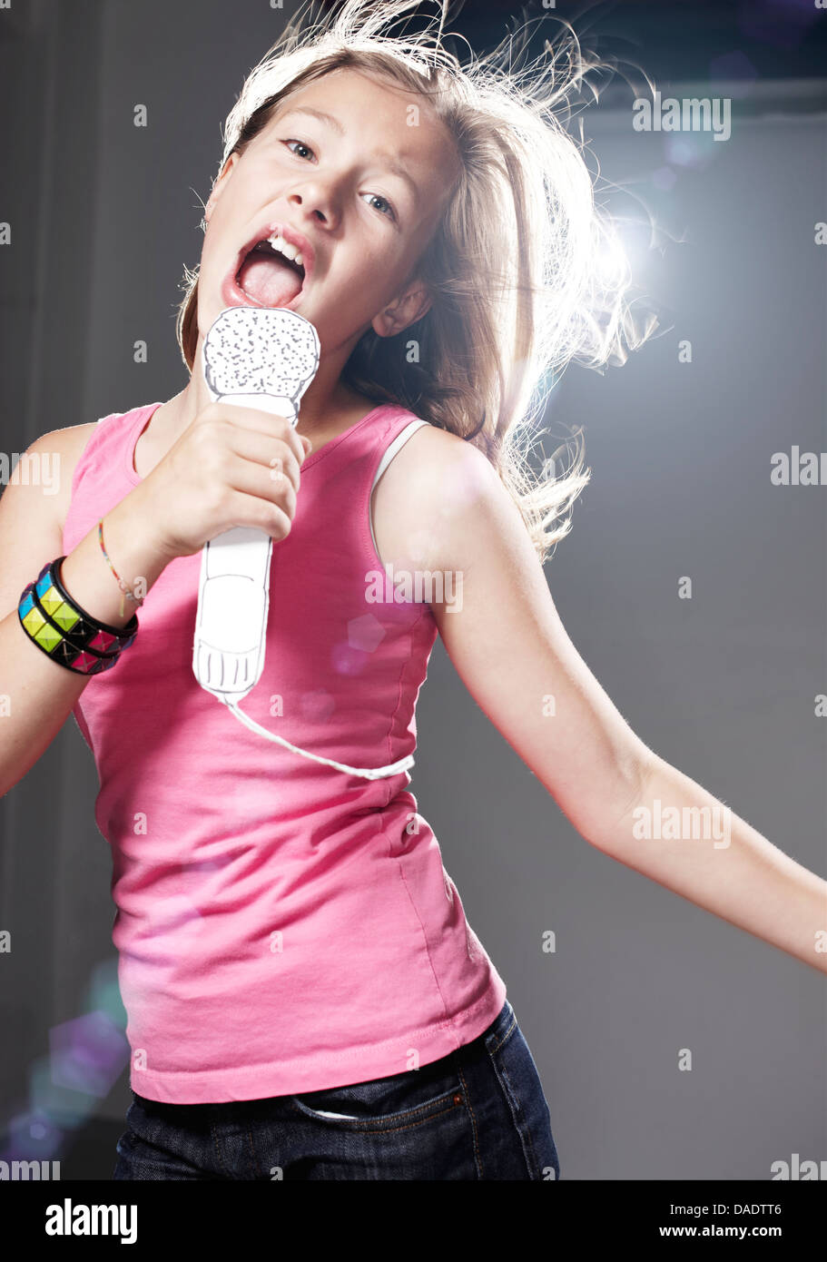 Girl en chantant dans le microphone contre l'arrière-plan gris papier Banque D'Images