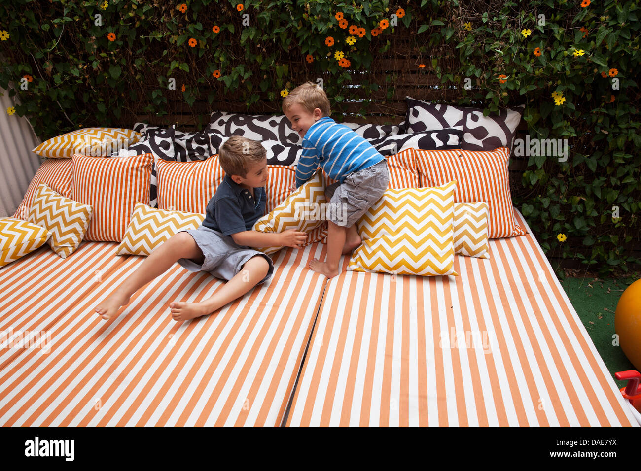 Deux garçons jouant sur du mobilier de jardin avec coussins Banque D'Images
