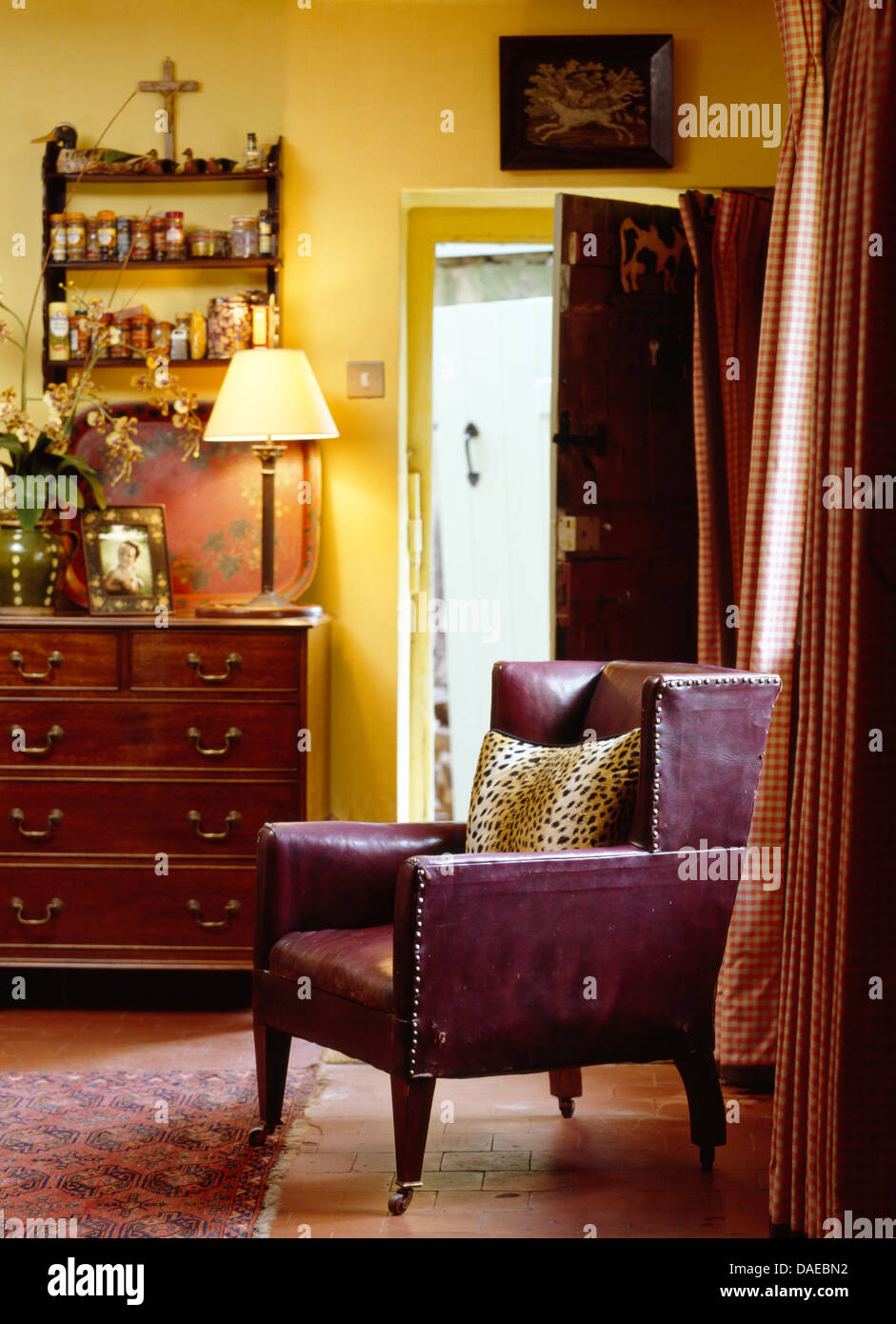 Fauteuil en cuir violet en jaune pays salon avec lampe allumée sur commode ancienne à côté de la porte ouverte Banque D'Images