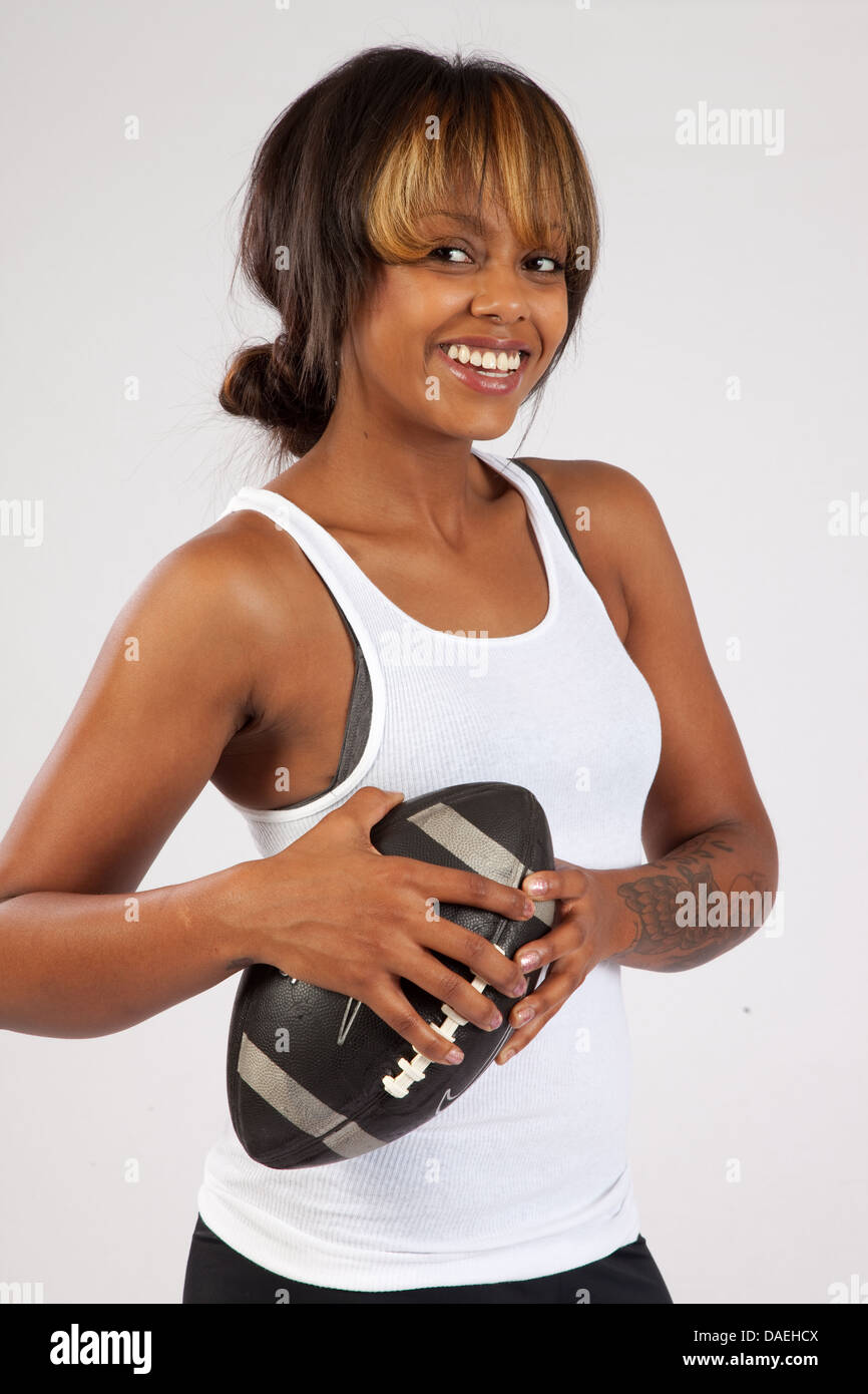 Jolie femme noire dans une camisole holding a football dans ses bras et souriant à la caméra avec un sourire heureux Banque D'Images