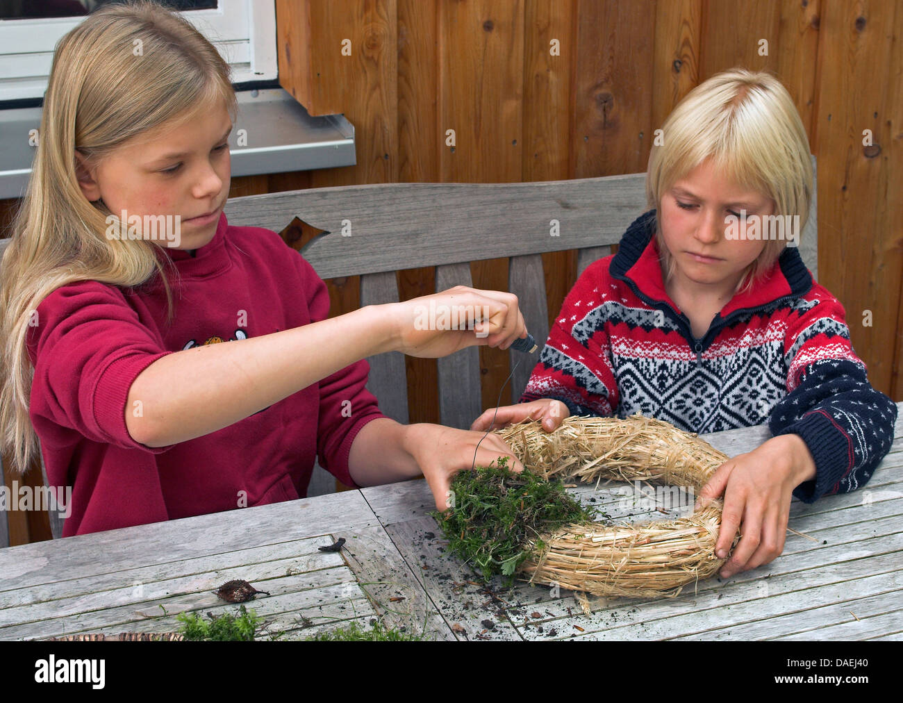Garçon et fille avec mousse de liage du fil à une gerbe de paille pour l'Avent, Allemagne Banque D'Images
