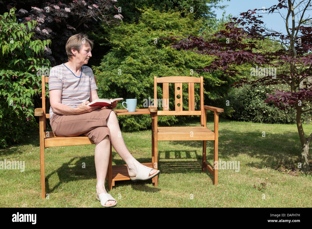 Hauts femme veuve de baby-boomers à la triste et solitaire assis seul à côté d'un compagnon vide siège dans un jardin ensoleillé en été. UK Banque D'Images