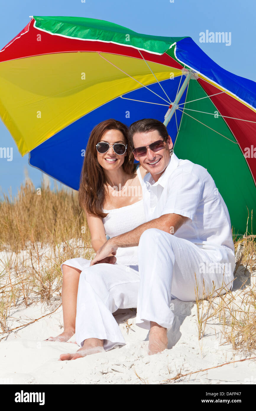 L'homme et la femme couple portant des lunettes de soleil sous un parasol  de couleur ou d'un parasol sur une plage Photo Stock - Alamy