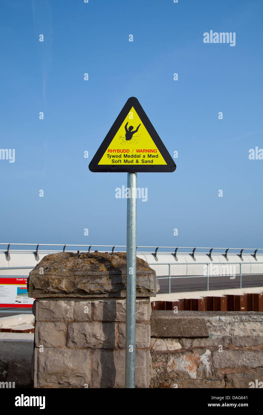 Gallois bilingue anglais / Panneau d'avertissement - boue molle & Sand à Voryd / Foryd Harbour avec les défenses de la mer en arrière-plan Banque D'Images