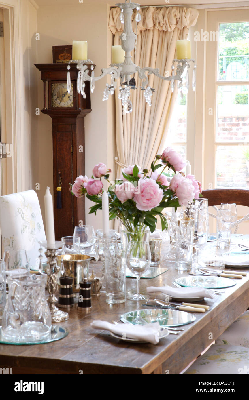 Le tableau ci-dessus en verre de définir pour le déjeuner avec vase de pivoines rose en pays salle à manger avec portes-fenêtres sur rideaux crème Banque D'Images