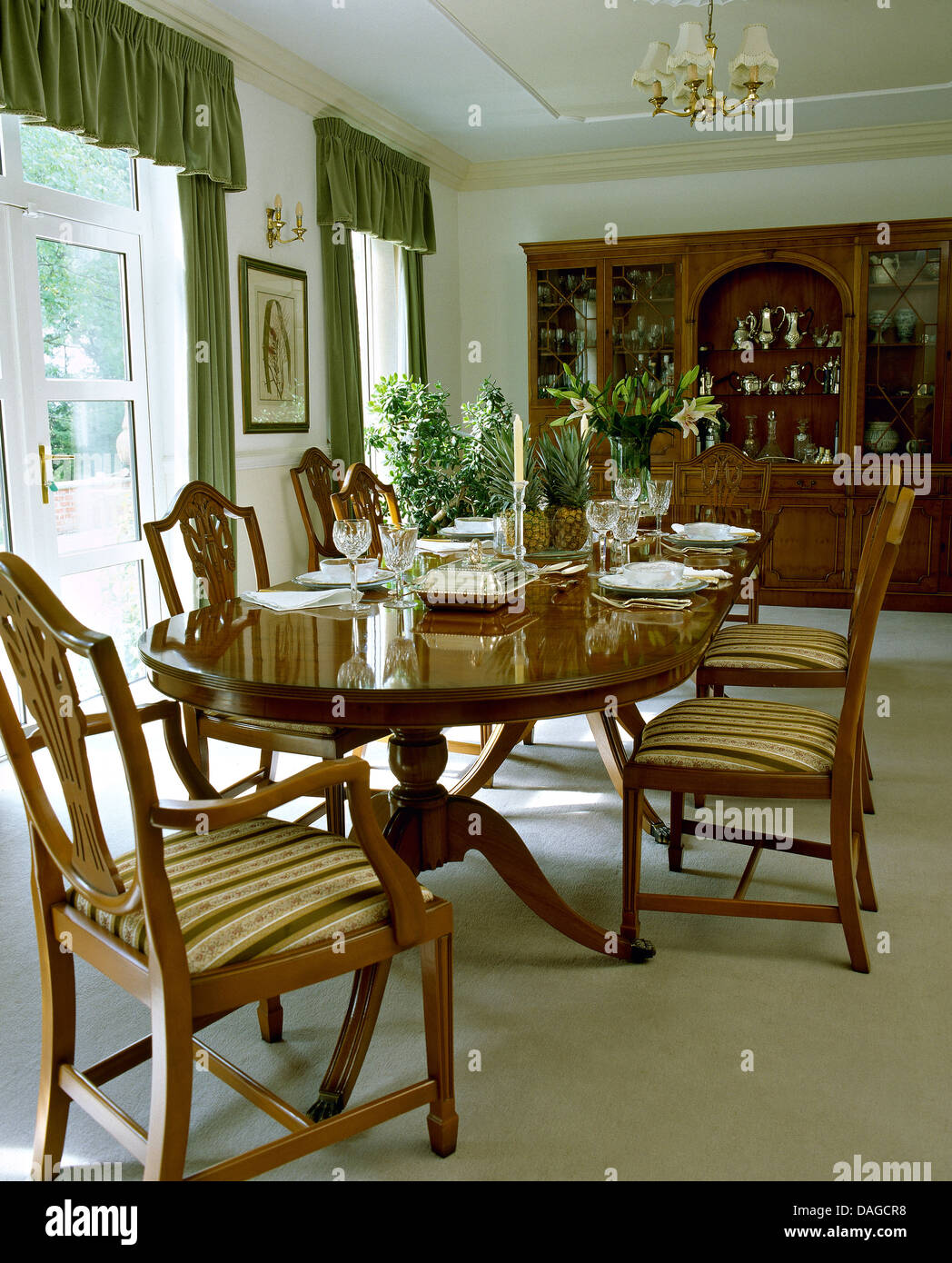 Table en acajou ovale et de confortables chaises de style Chippendale en pays salle à manger avec tapis blanc et rideaux verts Banque D'Images