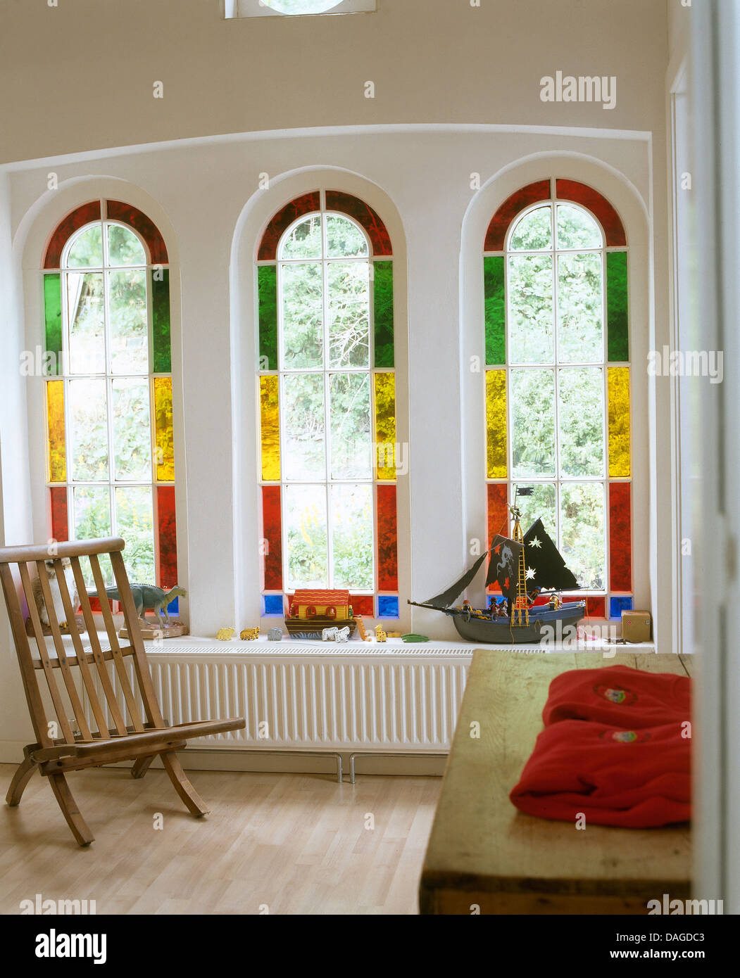 Vitraux fenêtres cintrées sur chant long au-dessus du radiateur, avec chaise en bois et la poitrine en chapelle convertie Banque D'Images