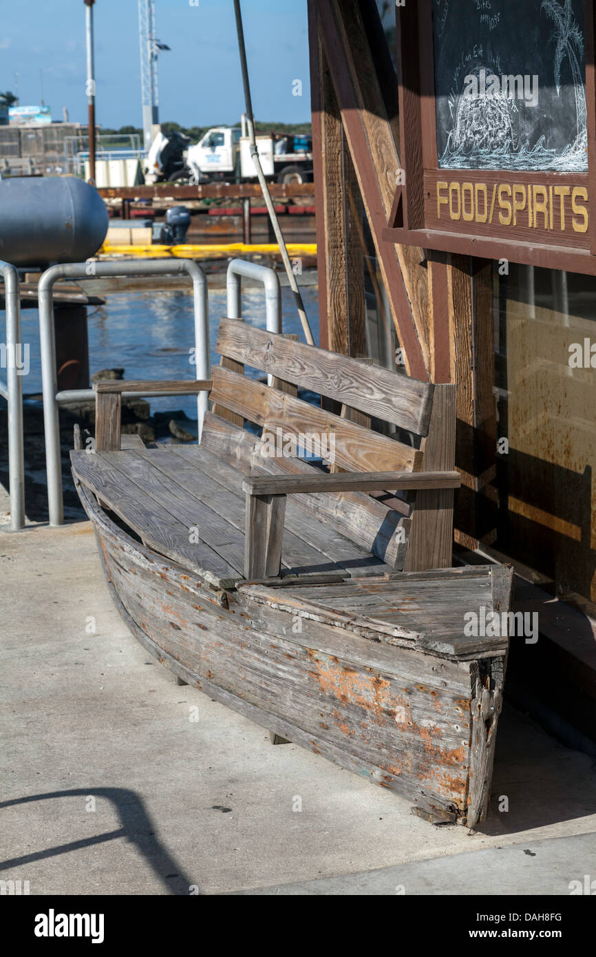 Battre en forme de bateau en bois banc en face d'un établissement au bord de l'alimentation et la publicité des spiritueux. Construction de quais visibles. Banque D'Images
