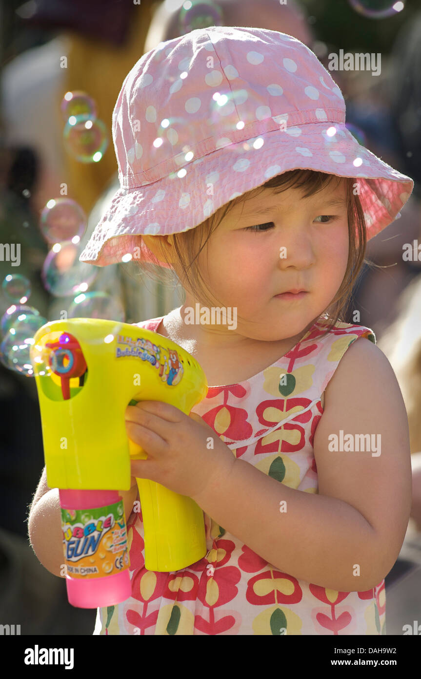 Parution du modèle. Jeune fille de 2 ans faire des bulles avec un pistolet à bulle. Brighton et Hove, Angleterre Banque D'Images