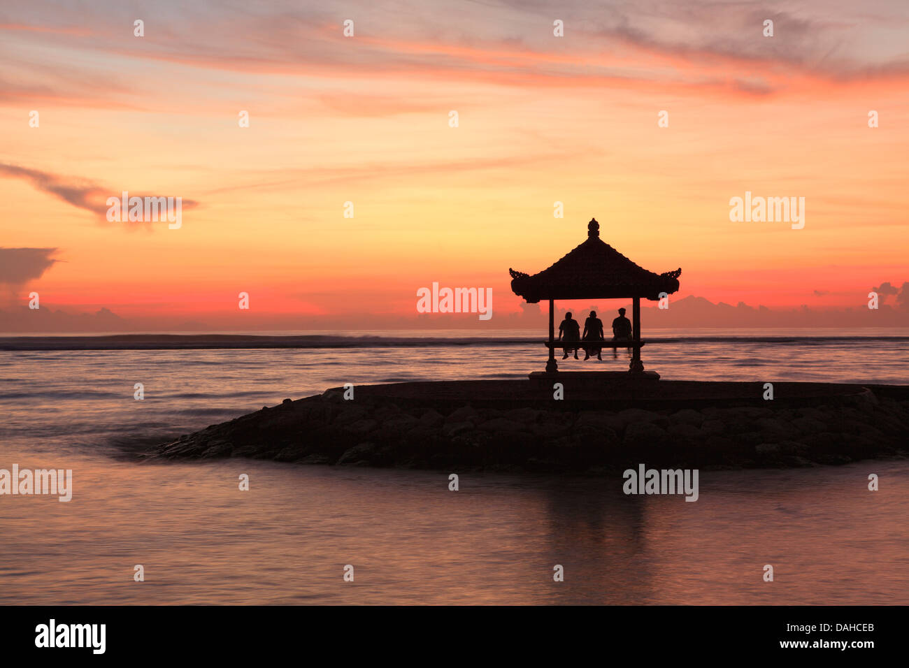 Trois personnes dans une pagode balinais sur la plage de Sanur, Bali. Prises à l'aube. Bali, Indonésie Banque D'Images