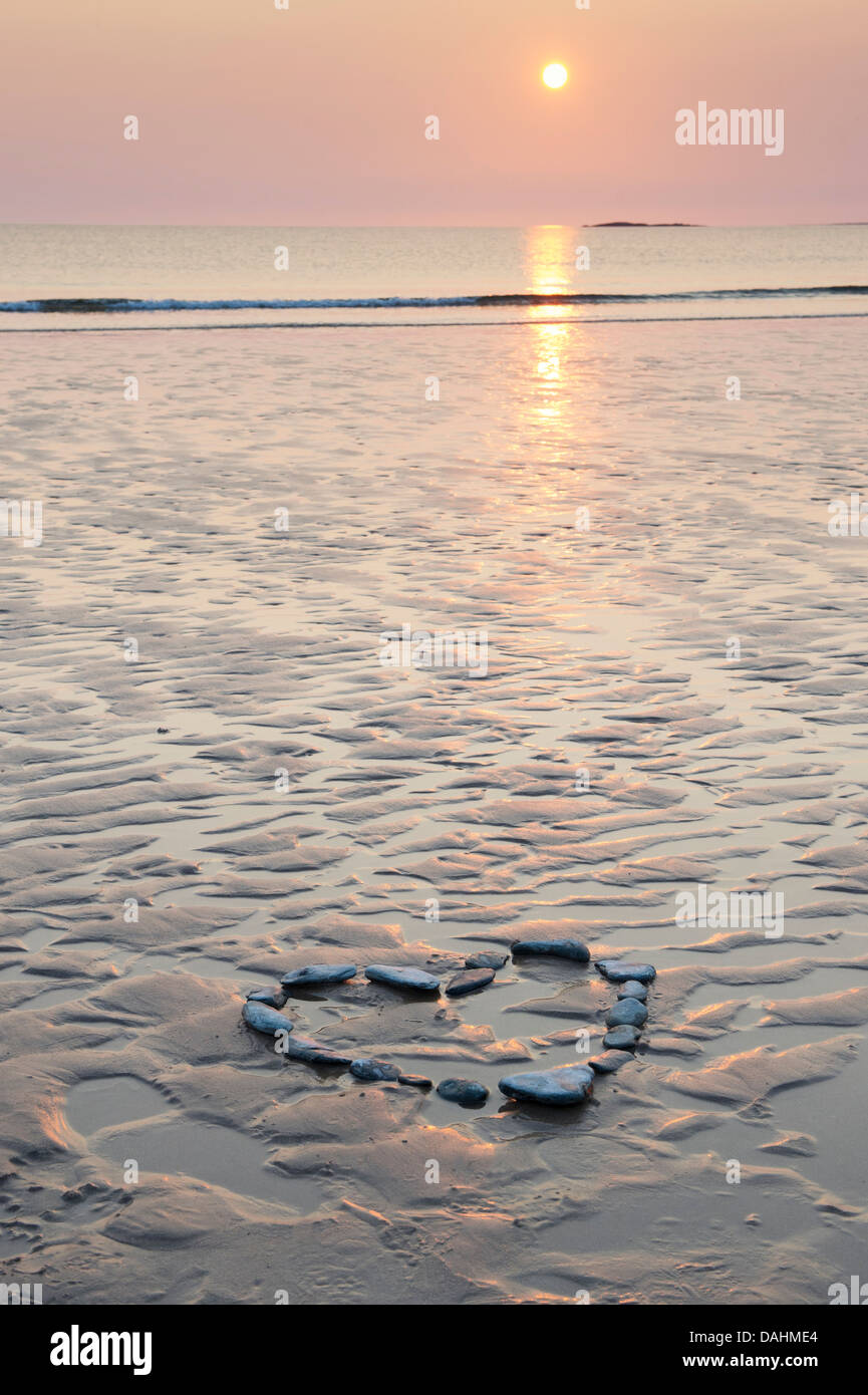 Forme de coeur galets sur une plage au lever du soleil. UK Banque D'Images