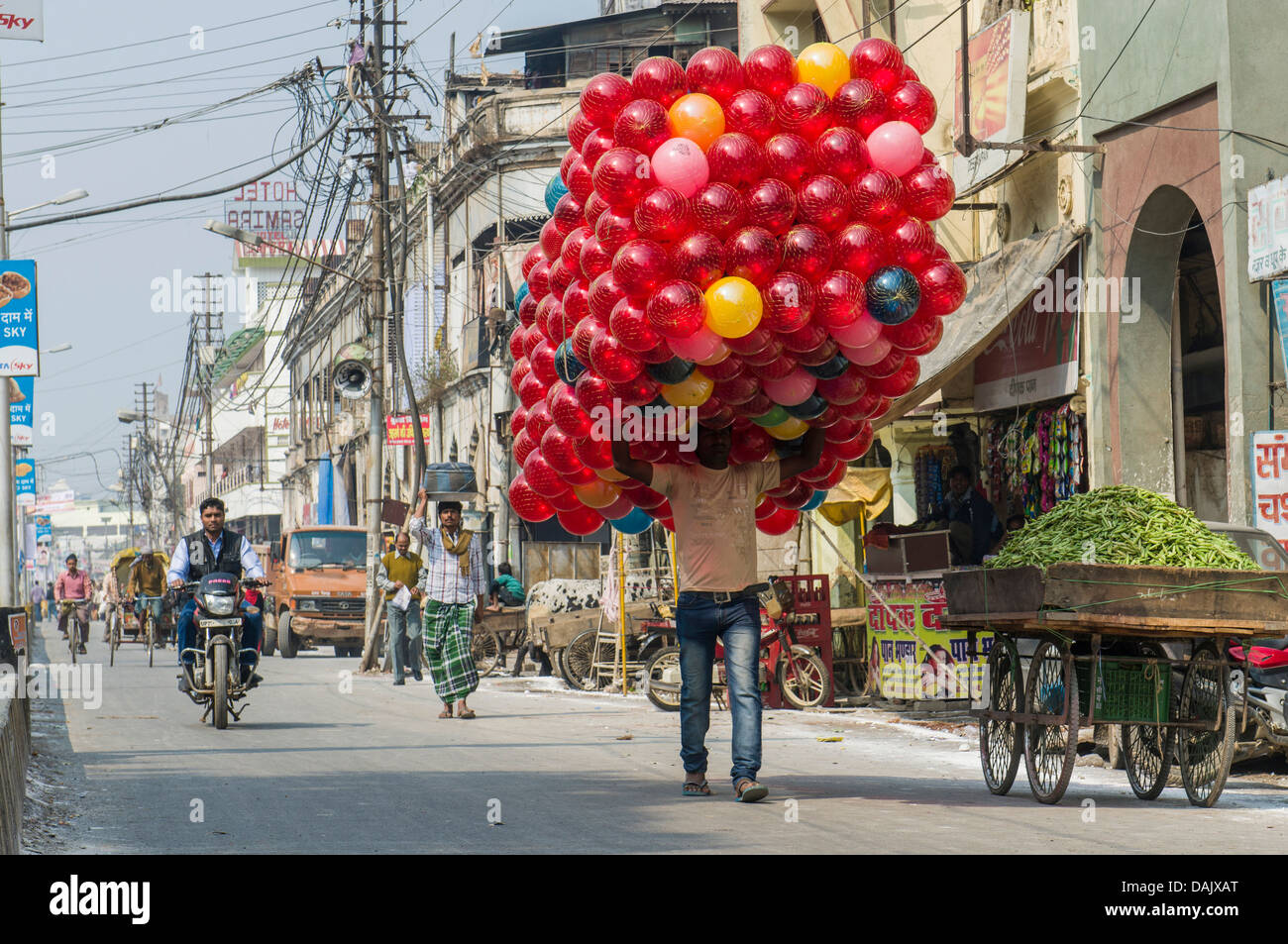 Homme portant un énorme paquet de balles jouet rouge le long d'une rue Banque D'Images