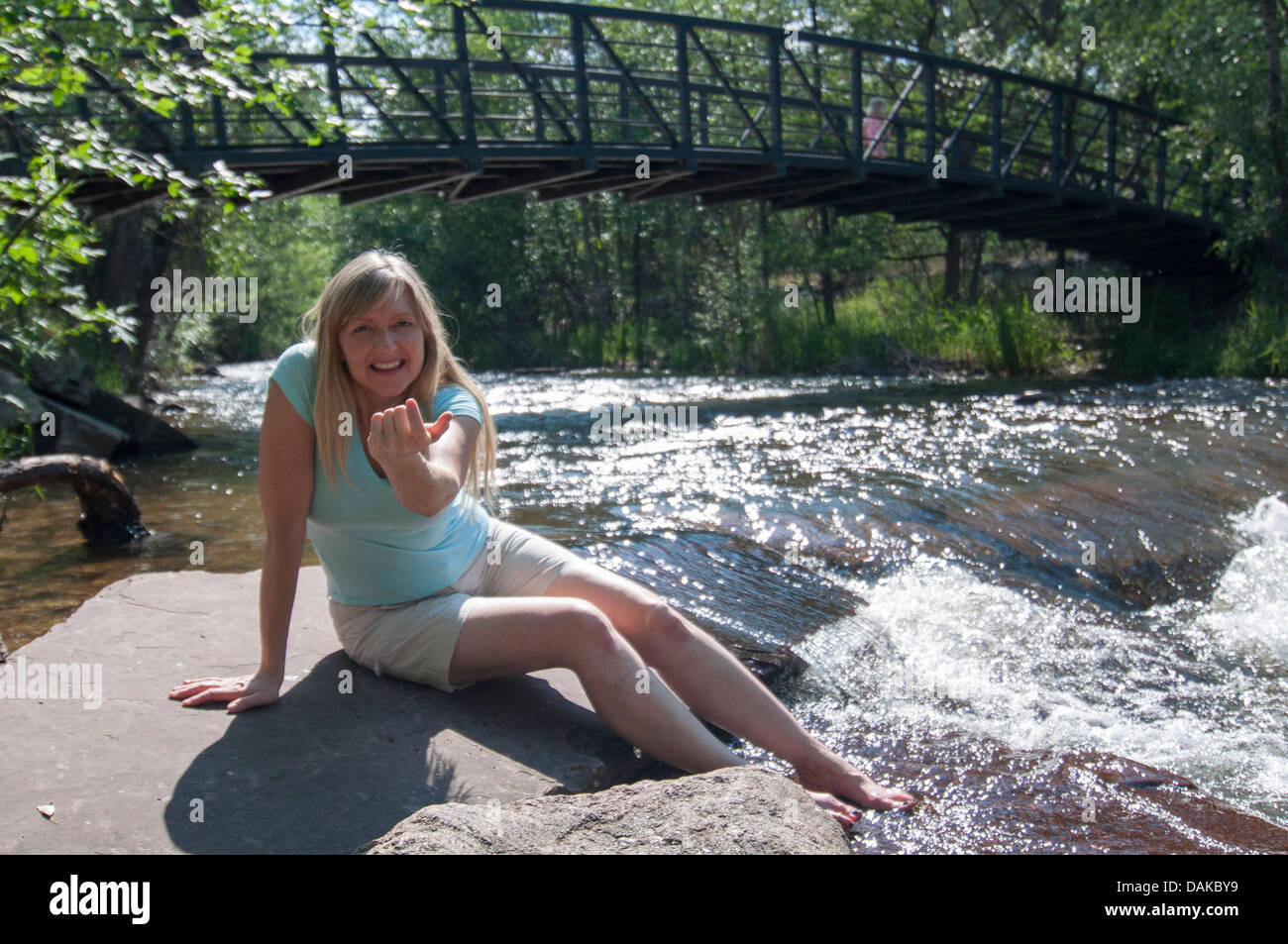 Femme assise sur la roche par la rivière s'invitant à venir rejoindre son appareil photo. Banque D'Images