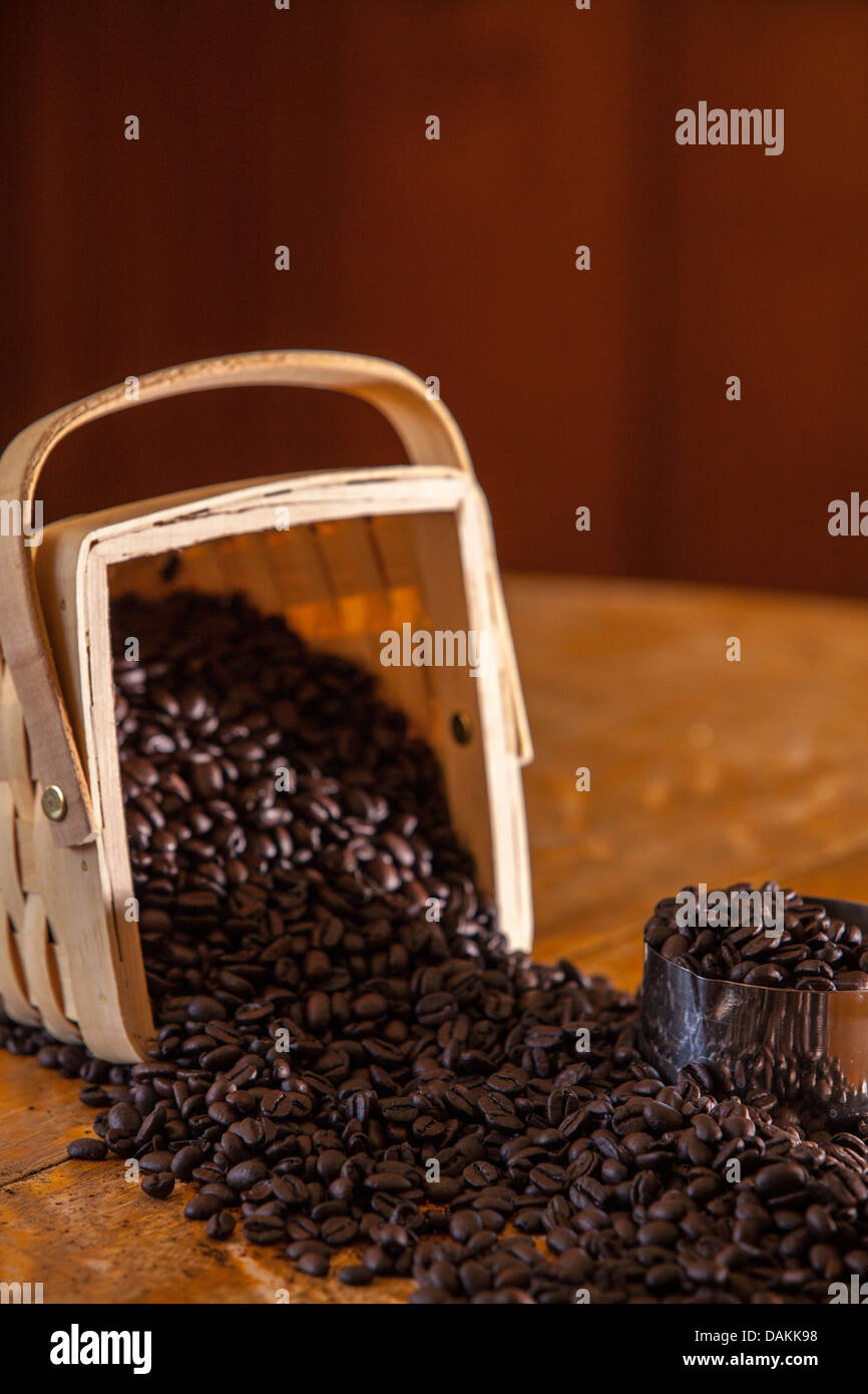 Les grains de café se répandre à partir d'un panier de bois sur une ancienne table en chêne Banque D'Images