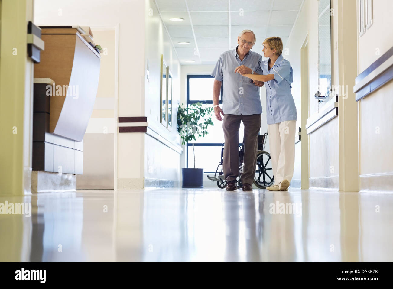 Aider l'infirmière à pied patient in hospital hallway Banque D'Images