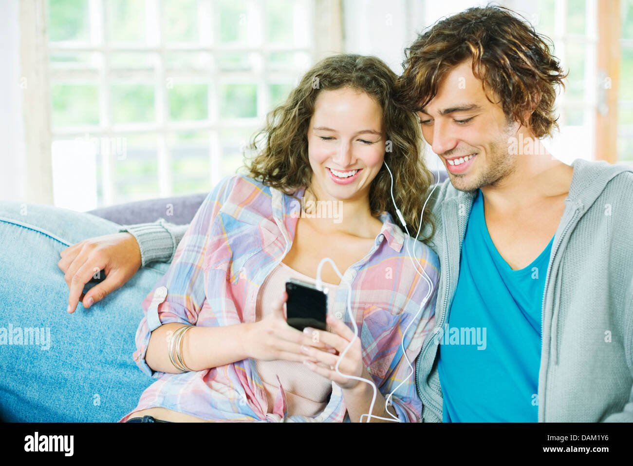Couple listening to earphones ensemble sur canapé Banque D'Images
