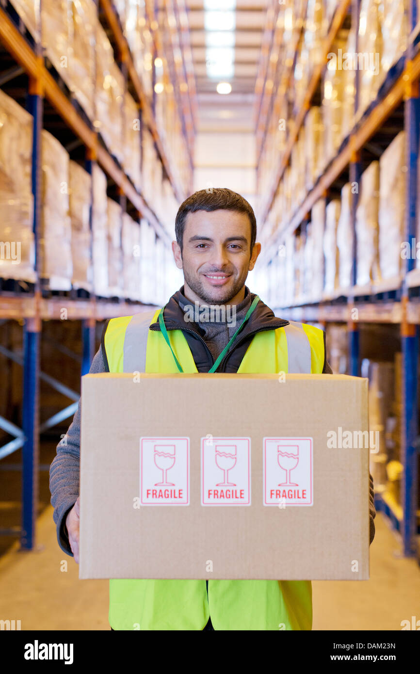 Worker carrying 'fragile' box in warehouse Banque D'Images