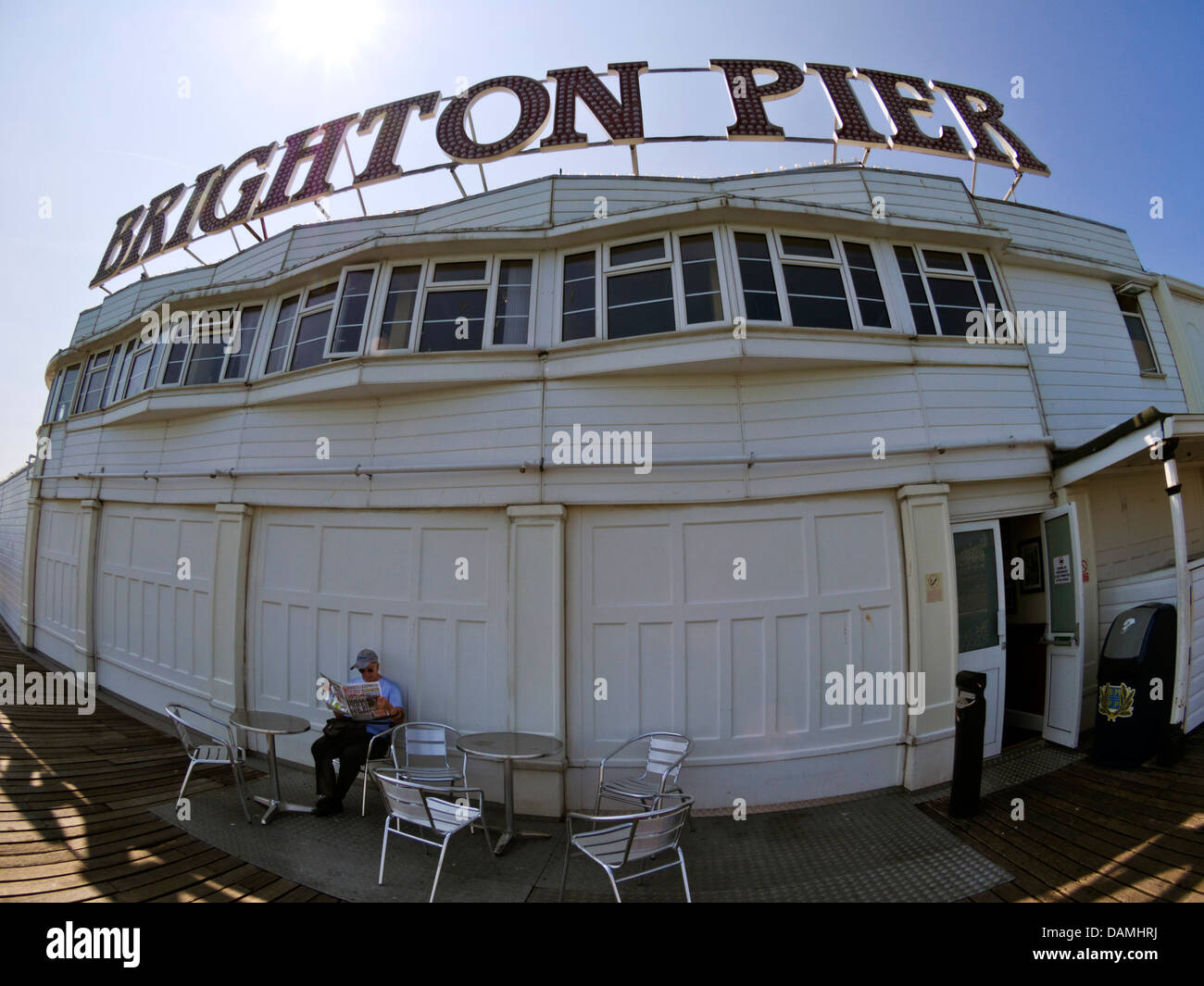 La mise à l'abri du soleil sur la jetée de Brighton pendant une vague - homme lecture Express journal dans l'ombre, prise grand angle Banque D'Images