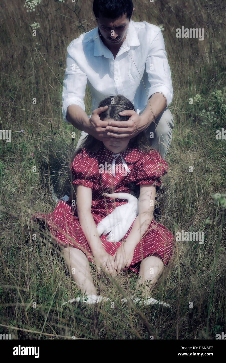Une fille est assise dans l'herbe, c'est l'homme tenant ses mains devant ses yeux Banque D'Images