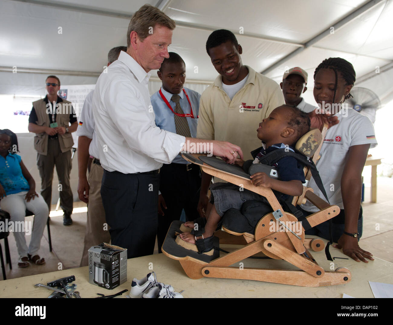 Le ministre des Affaires étrangères allemand Guido Westerwelle (L) accueille un garçon, qui se trouve à l'intérieur d'une chaise orthopédique, à l'aide de l'organisation Johanniter LÉOGÂNE, Haïti, 17 juillet 2011. La visite de l'état des Caraïbes est Westerwelle's dernier arrêt de sa tournée à travers l'Amérique latine. Photo : Soeren Stache Banque D'Images