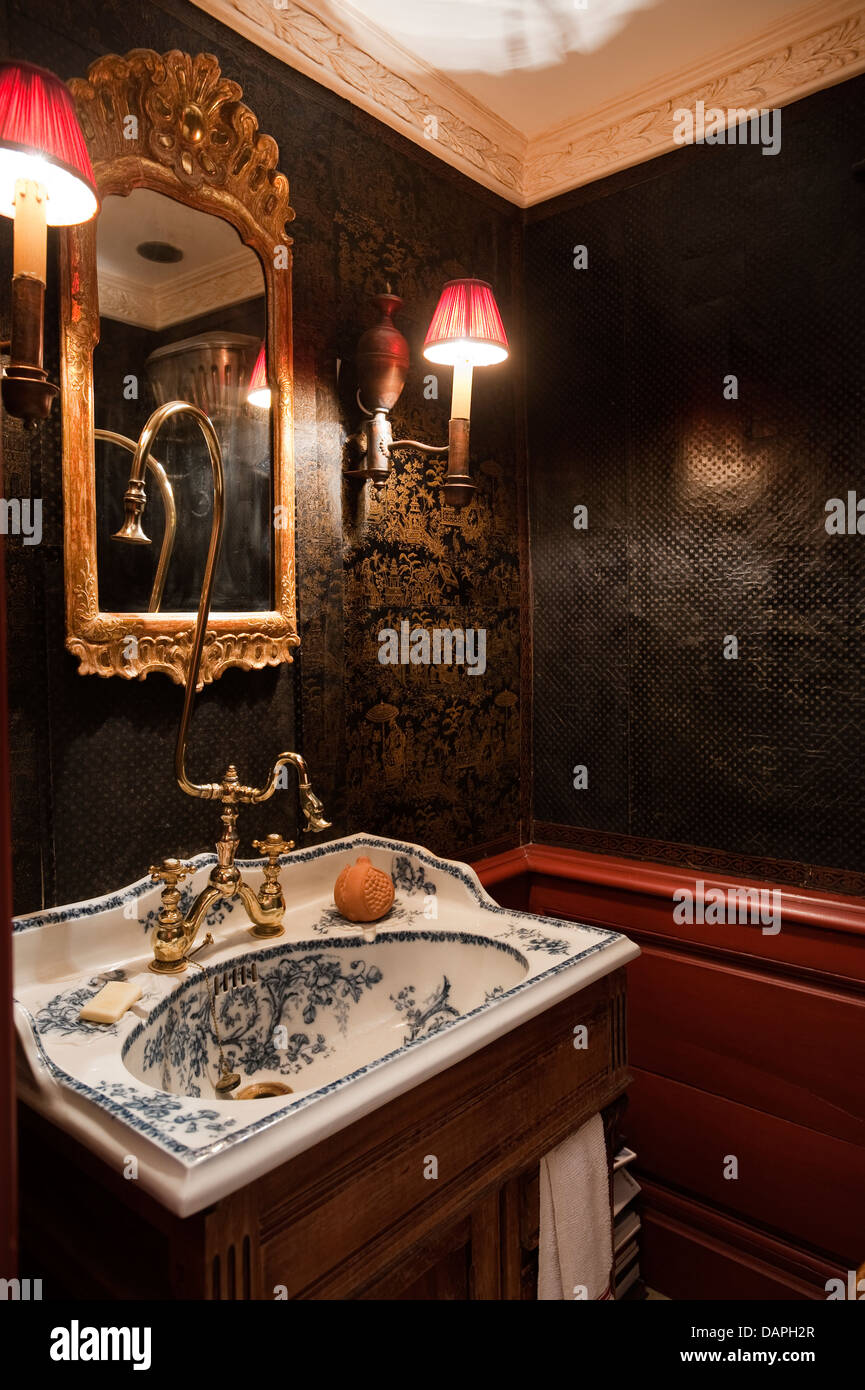 Un lavabo en porcelaine bleu et blanc et miroir doré flanqué d'appliques en abat-jour rouge Banque D'Images
