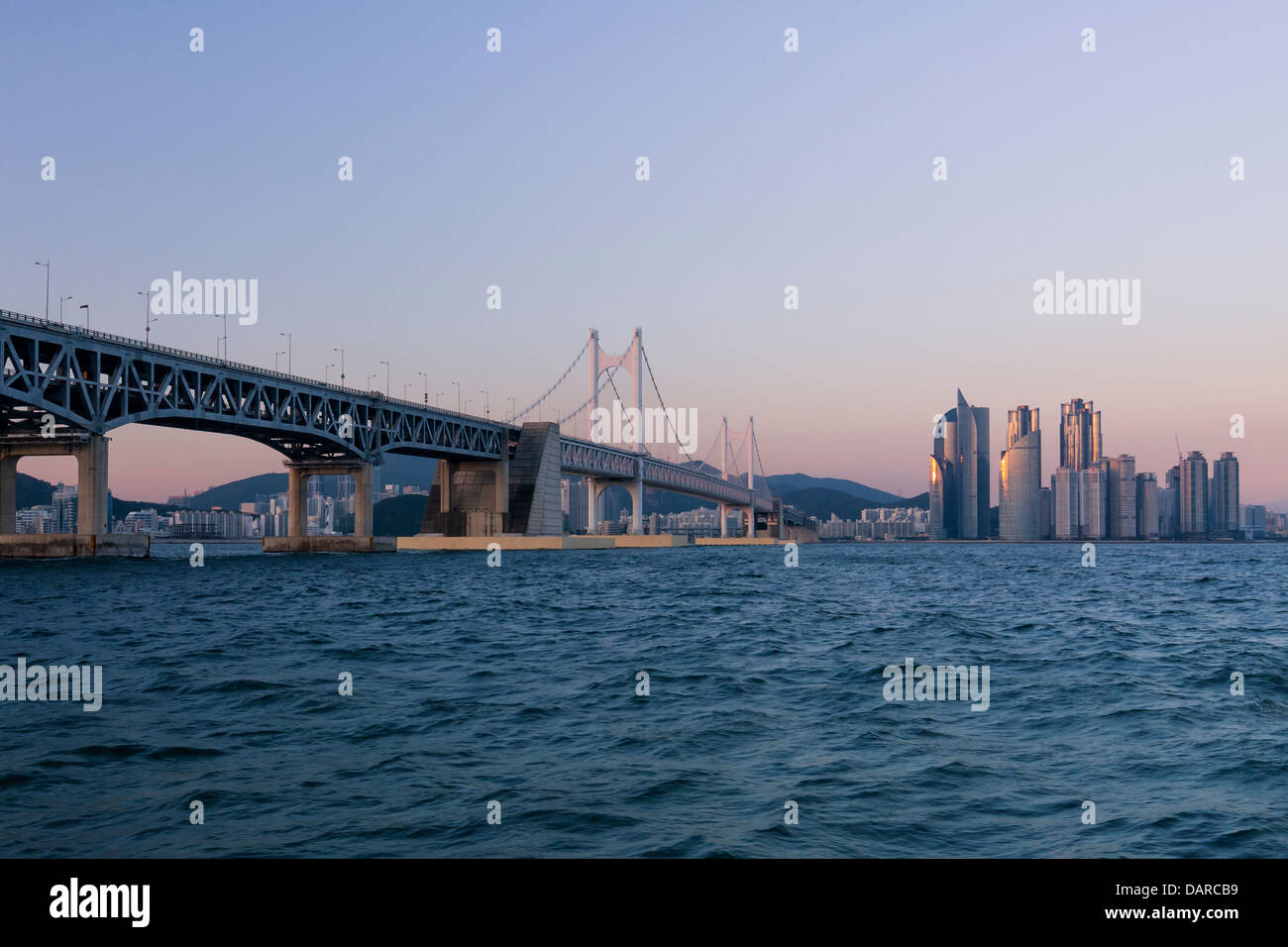 Les bâtiments résidentiels et d'hôtels à Haeundae, Busan, Corée du Sud et le pont Gwangan au crépuscule, vu de la mer. Banque D'Images