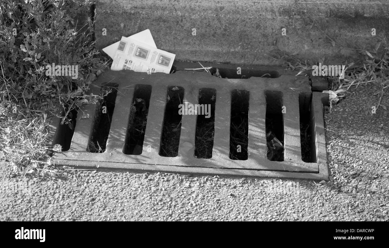 Une photographie en noir et blanc d'une vidange d'eau sur le côté sur une route avec une réception d'Aldi tombé dans c Banque D'Images