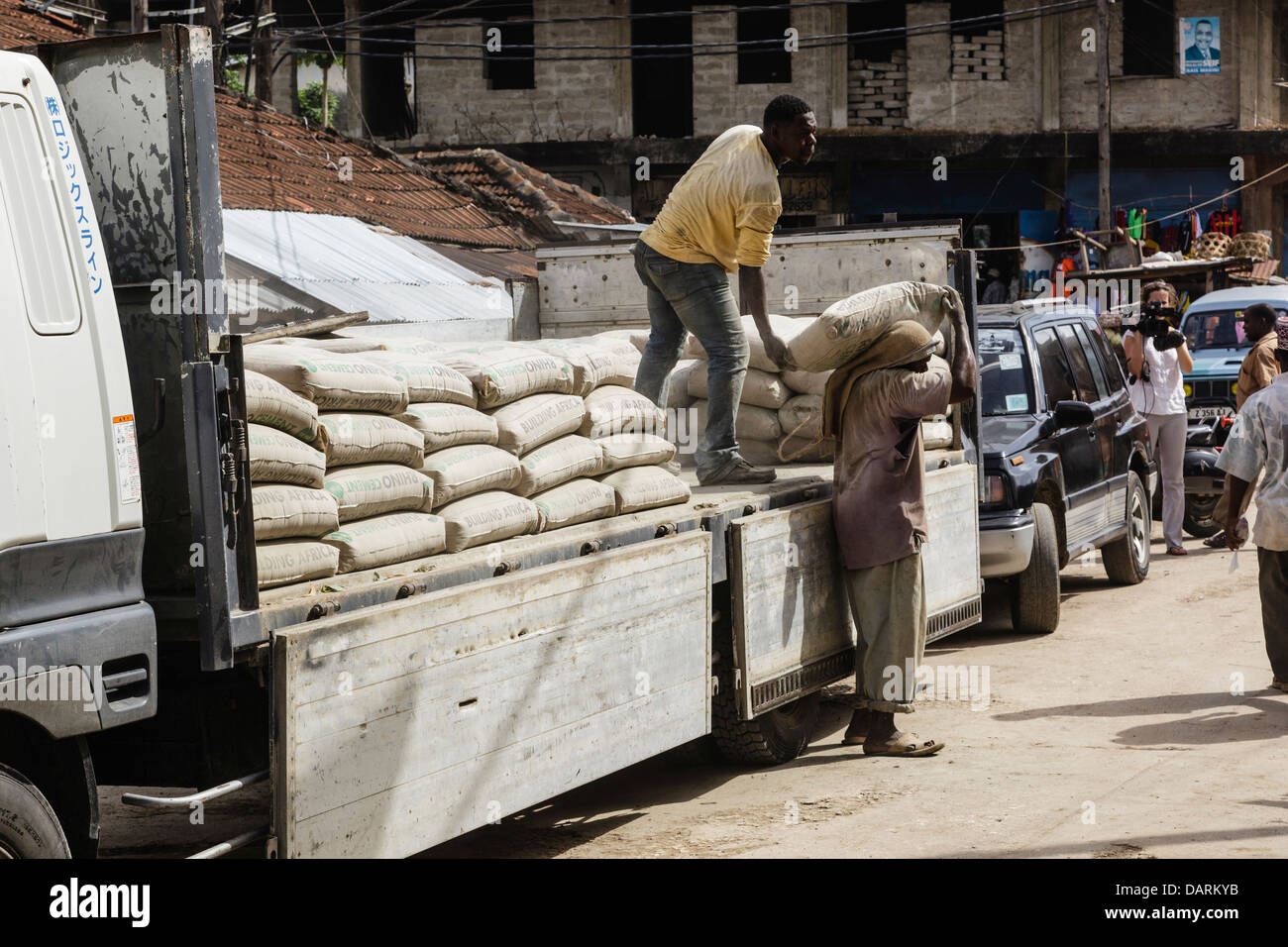L'Afrique, Tanzanie, Zanzibar, l'île de Pemba, Chake Chake. Les hommes le déchargement des sacs de béton sur rue. Banque D'Images