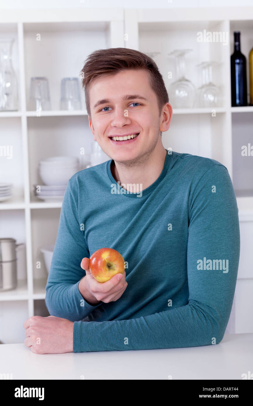 Jeune homme en bonne santé en mangeant une pomme dans sa cuisine moderne Banque D'Images