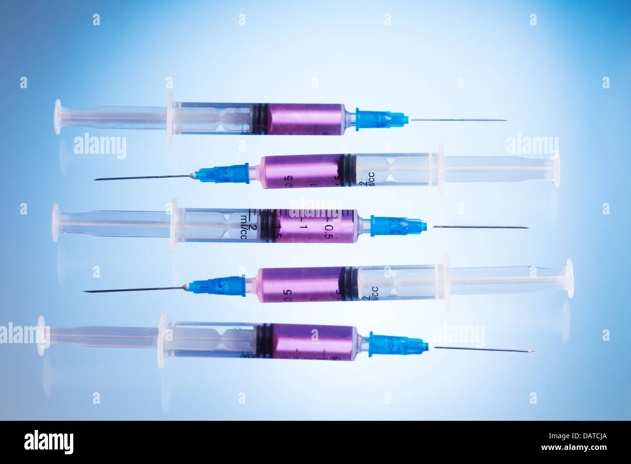 Cinq nouvelles seringues remplies de médicament rose sur le tableau bleu portant dans une rangée Banque D'Images