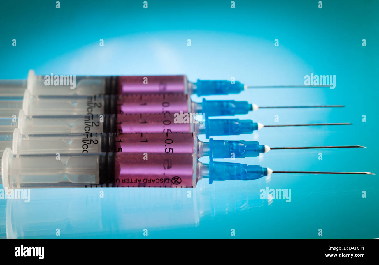 Cinq des seringues en plastique remplie de liquide rose sur le tableau bleu portant dans une rangée Banque D'Images