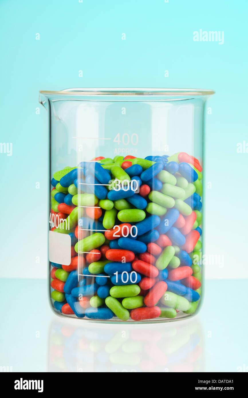 Récipient en verre de laboratoire avec vert bleu et rouge comprimés et comprimés sur bleu Banque D'Images