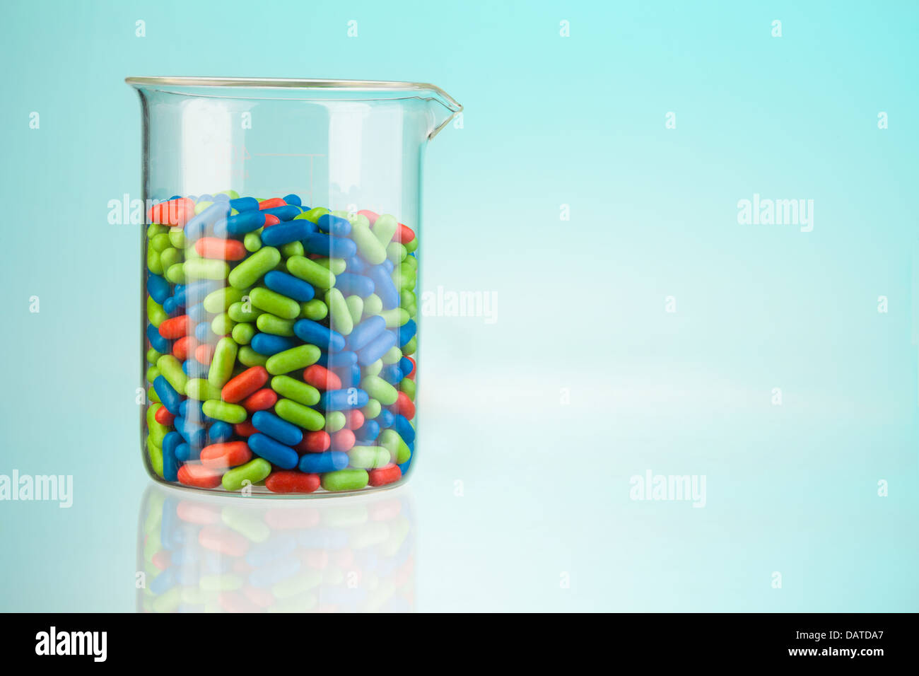 Récipient en verre de laboratoire avec vert bleu et rouge comprimés et comprimés sur bleu et copyspace Banque D'Images
