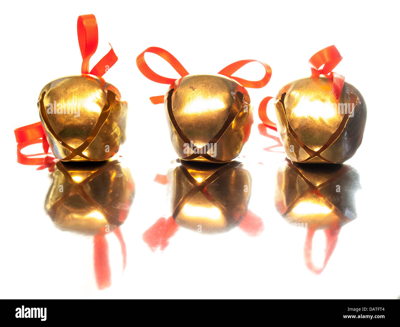 Trois brillant or sleigh bells avec petits nœuds rouge on reflective surface Banque D'Images