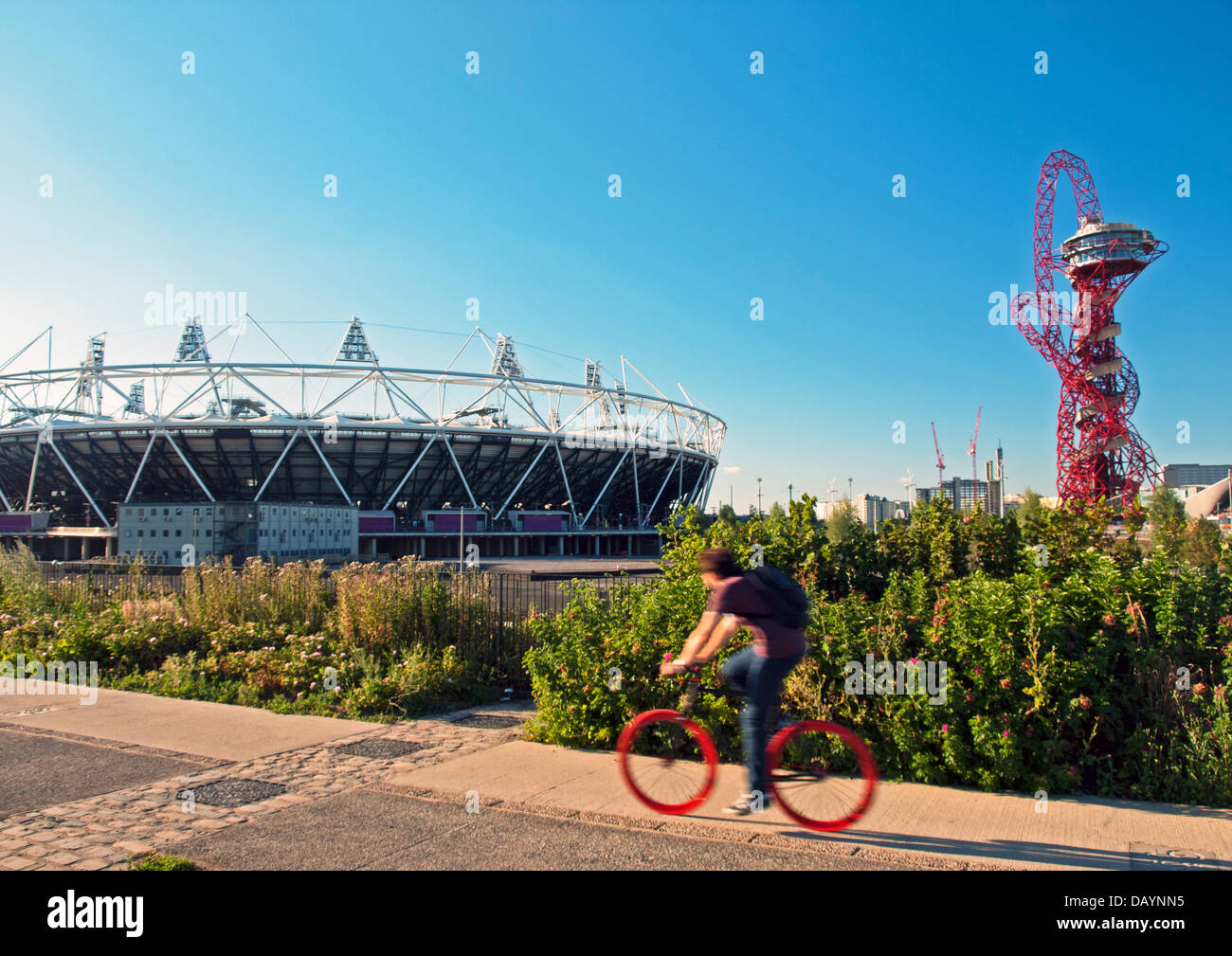 Un cycliste rides passé le stade olympique, stade de l'hôte pour l'été 2012 Jeux Olympiques et Paralympiques, et l'orbite d'ArcelorMittal Banque D'Images