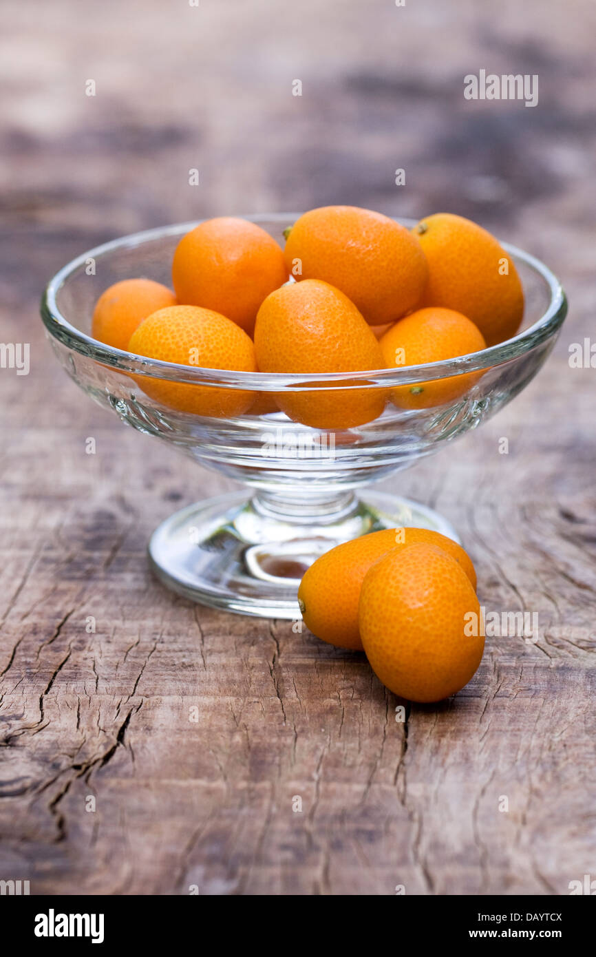 Les kumquats dans un bol en verre sur une planche de bois. Banque D'Images
