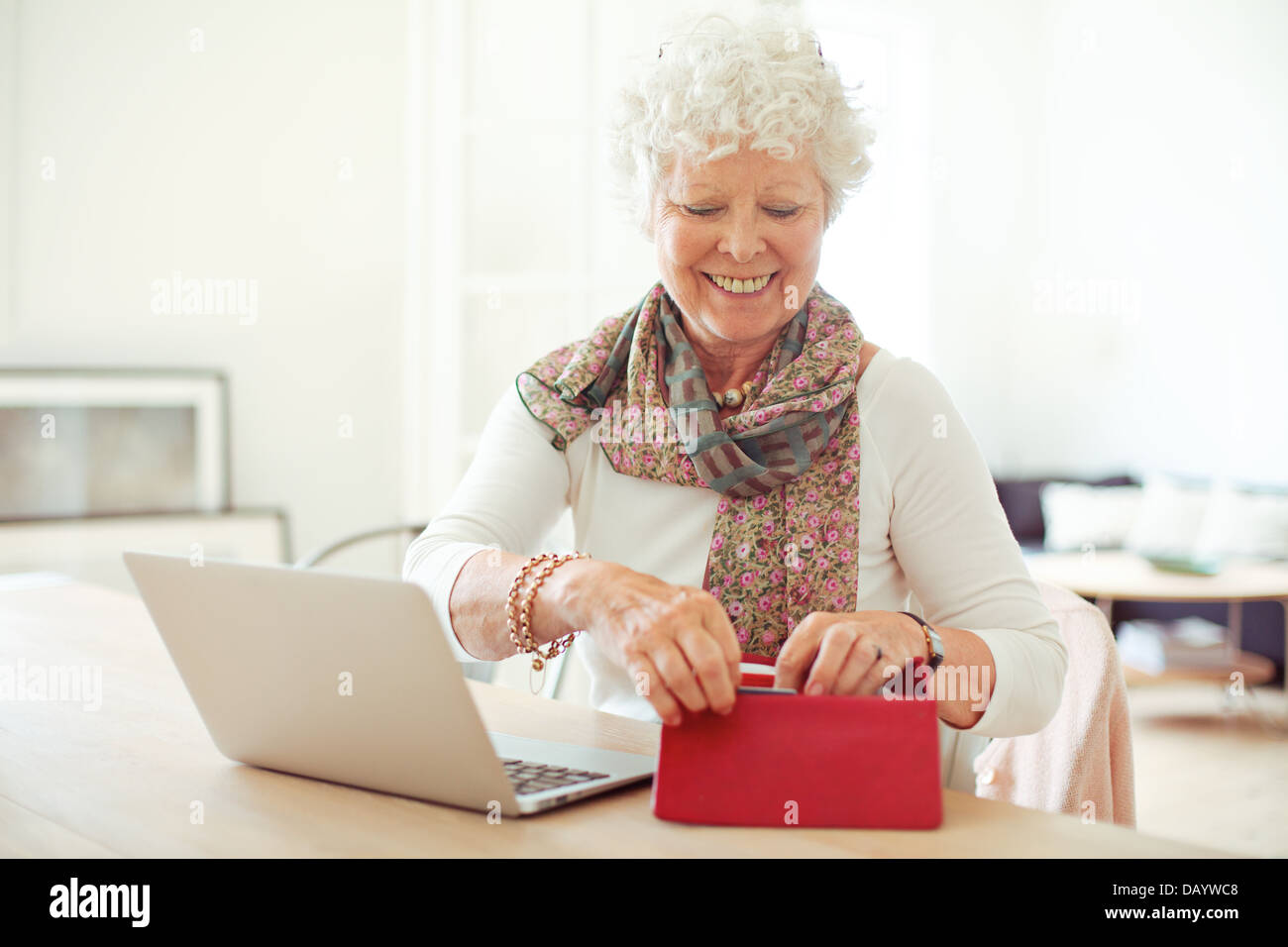 Cheerful old woman in front of laptop obtenir quelque chose de son portefeuille Banque D'Images