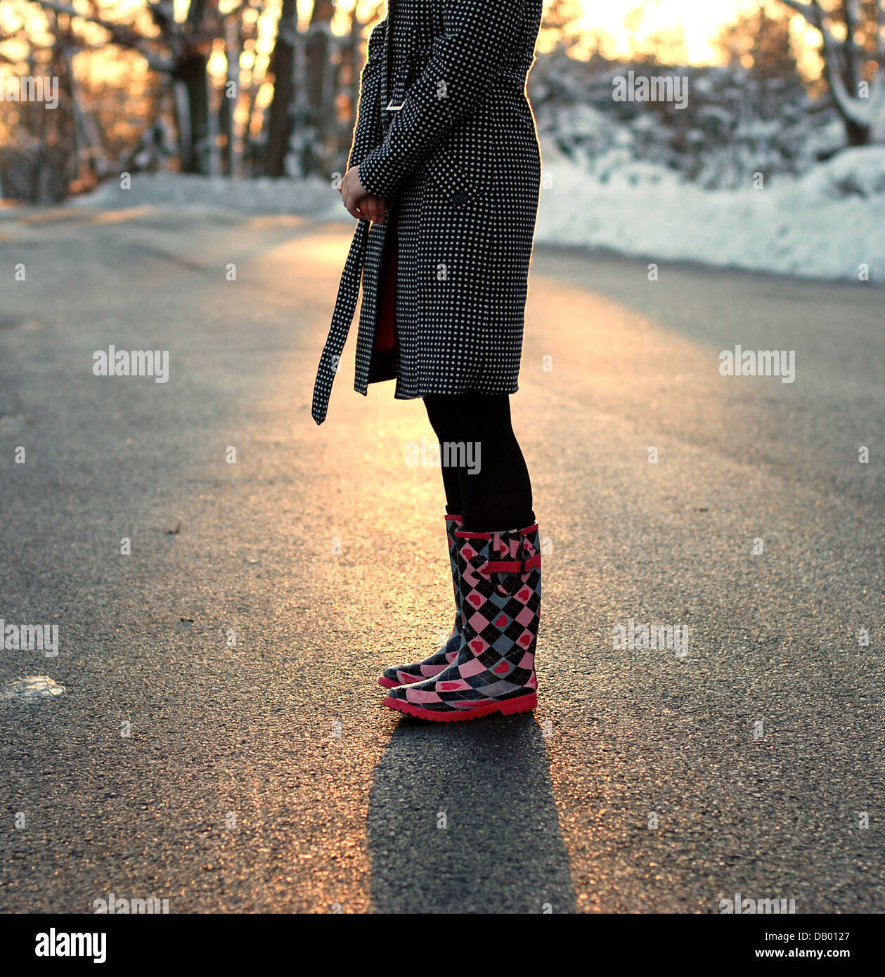 Une jeune fille portant des bottes de pluie / bottes de neige se dresse au  milieu de la rue pendant la Golden Hour coucher du soleil en hiver Photo  Stock - Alamy