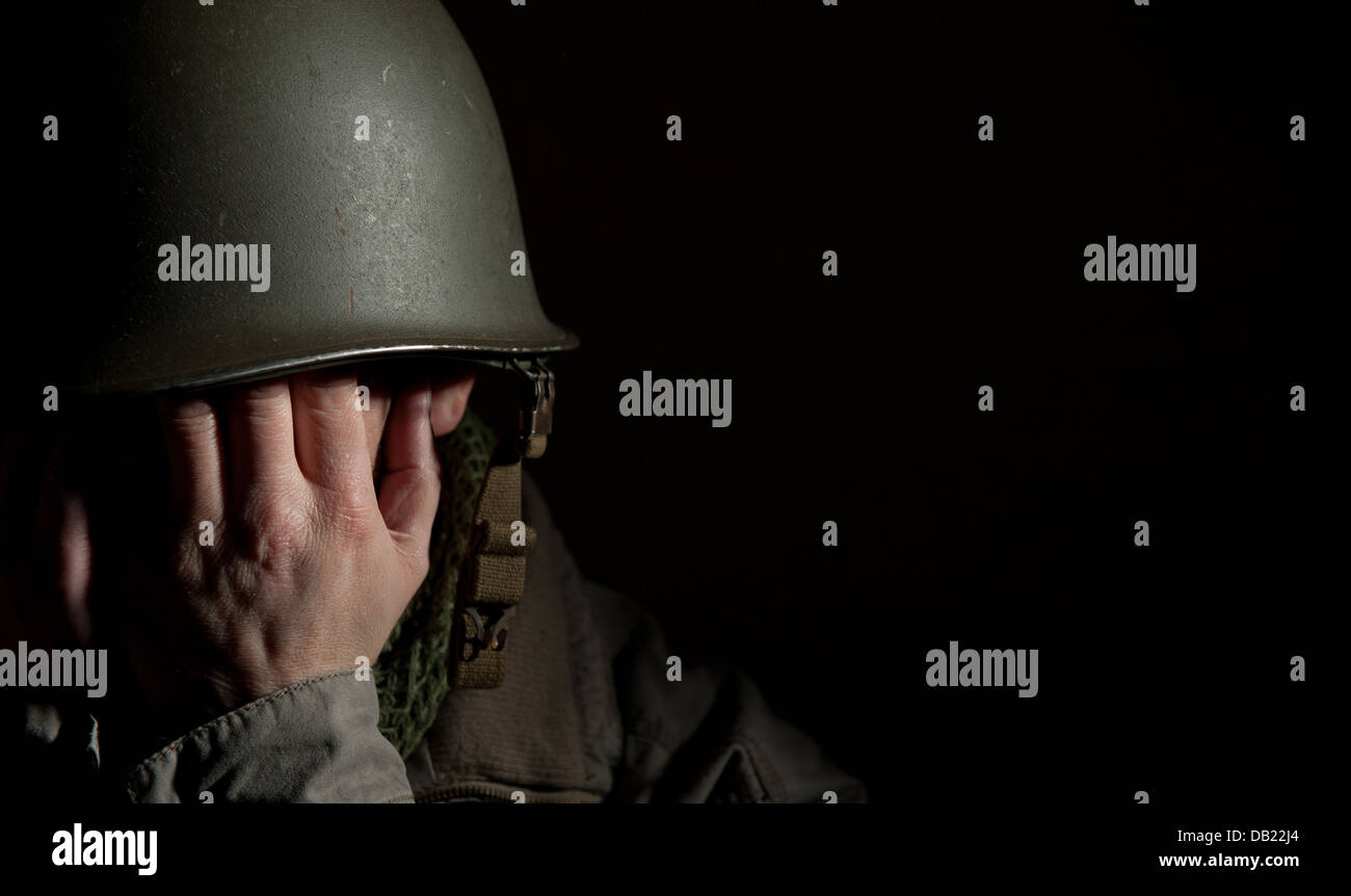 WW2 soldat américain P.T.S.D. avec souffrance et en utilisant ses mains pour couvrir son visage. Moody et spectaculaire contre un black b/g. Banque D'Images