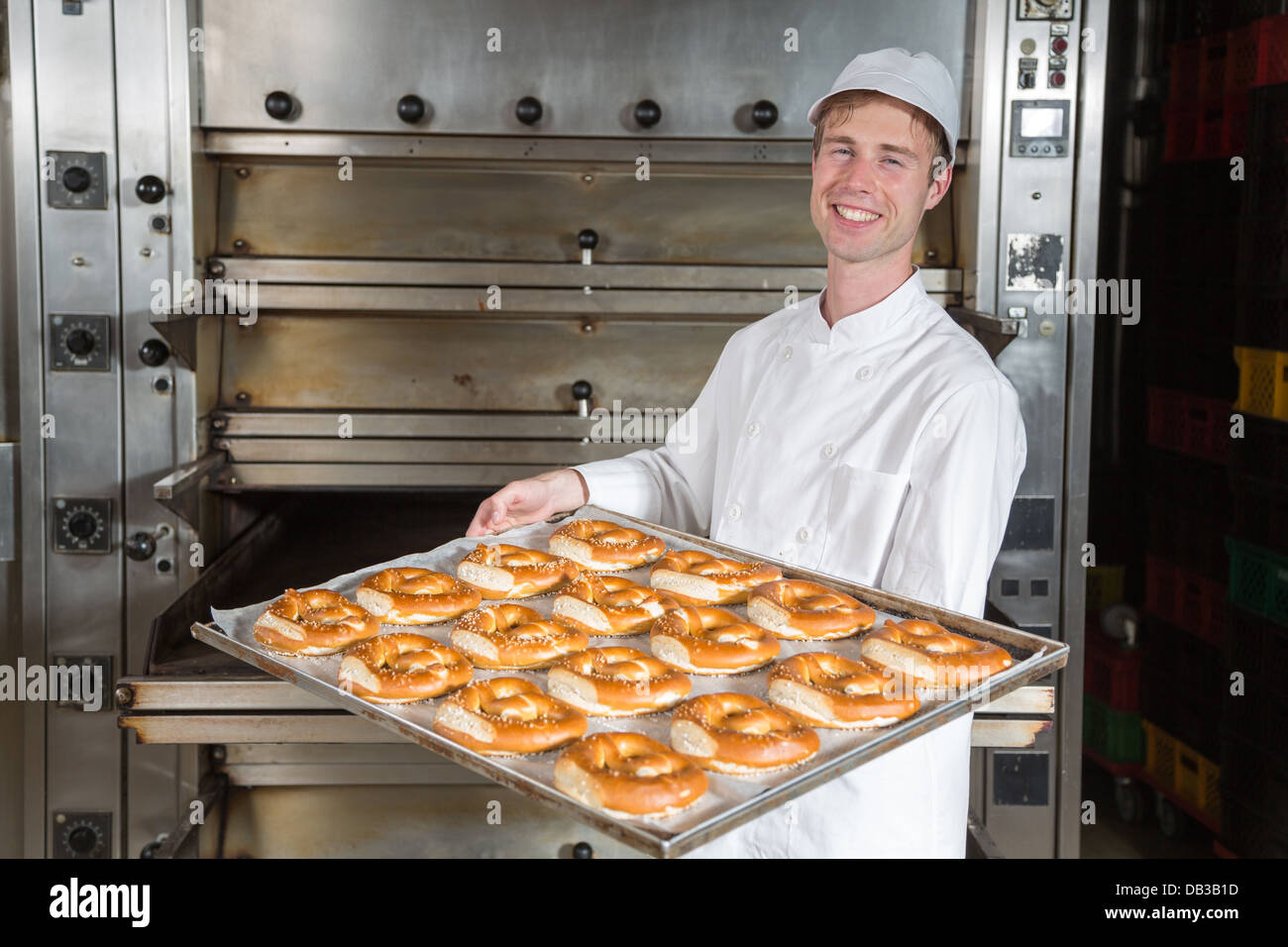 Baker posant avec cuisson plein de bretzels en face du four Banque D'Images