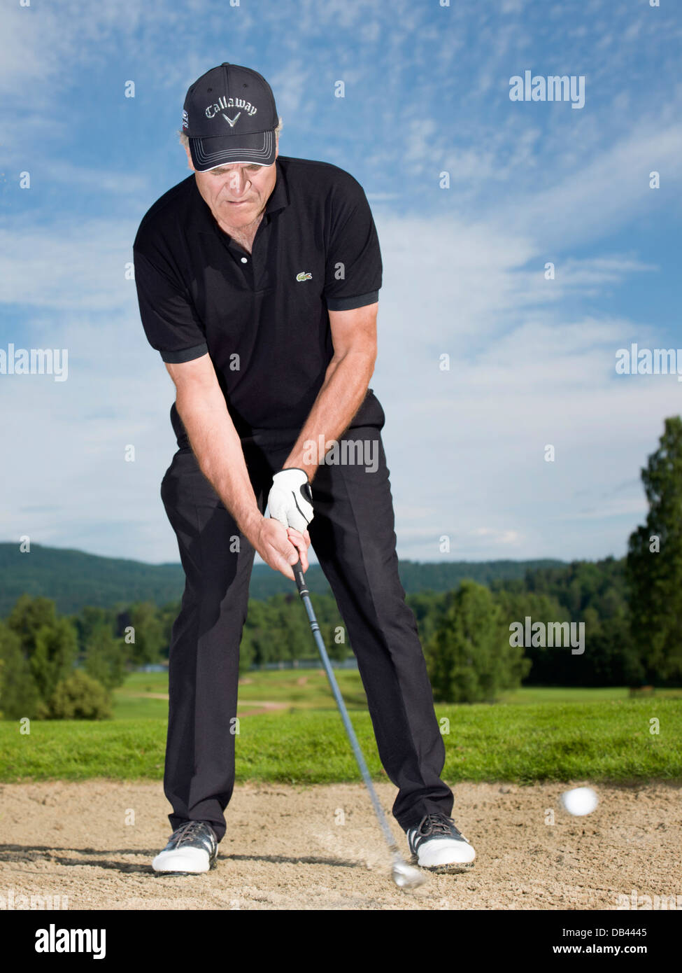 Senior citizen à jouer au golf, vêtus de noir. Photo d'action dans le bunker. Banque D'Images