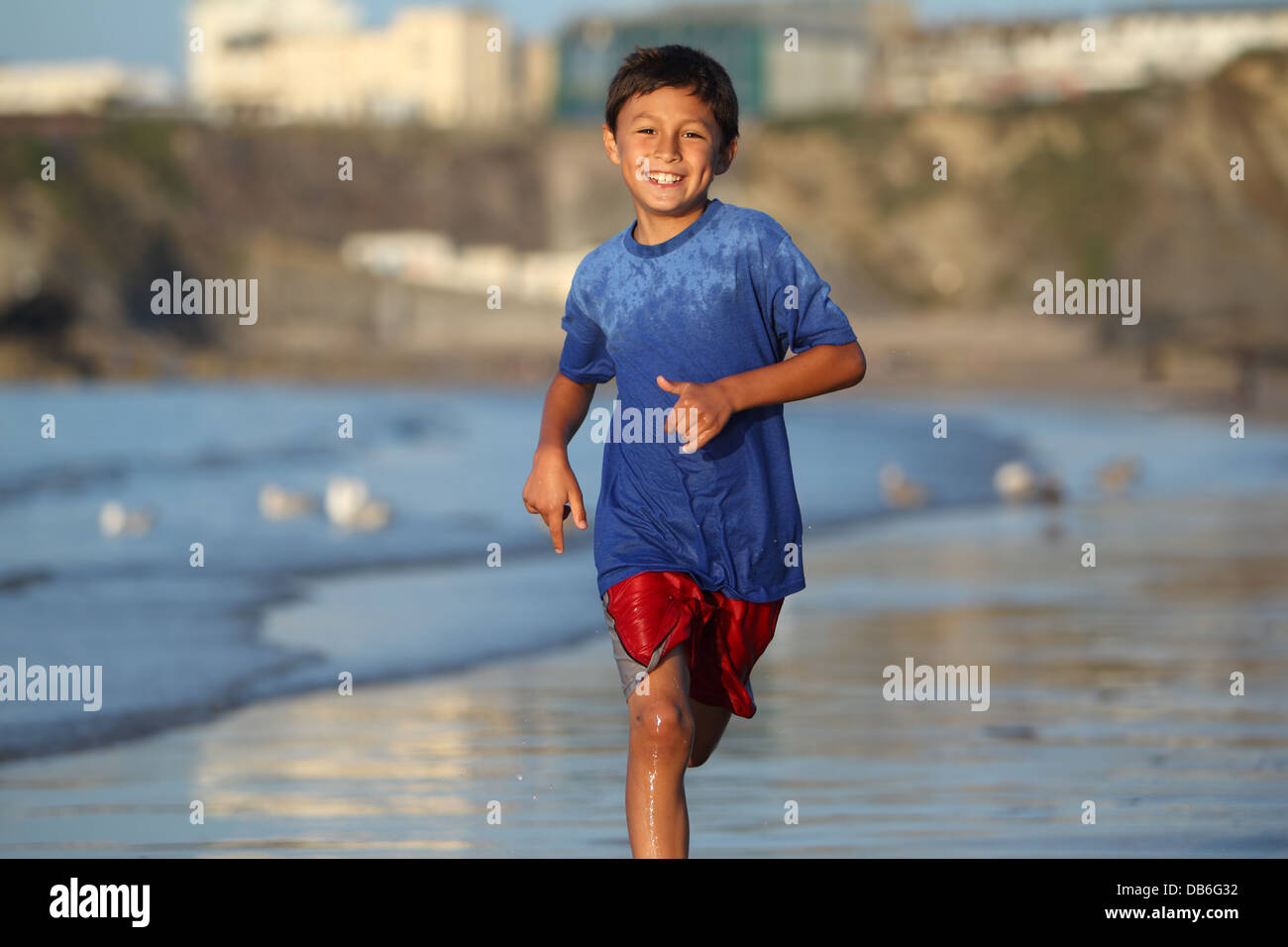 Jeune garçon joue et s'exécute dans le surf le long d'une plage anglaise près de Sunset Banque D'Images