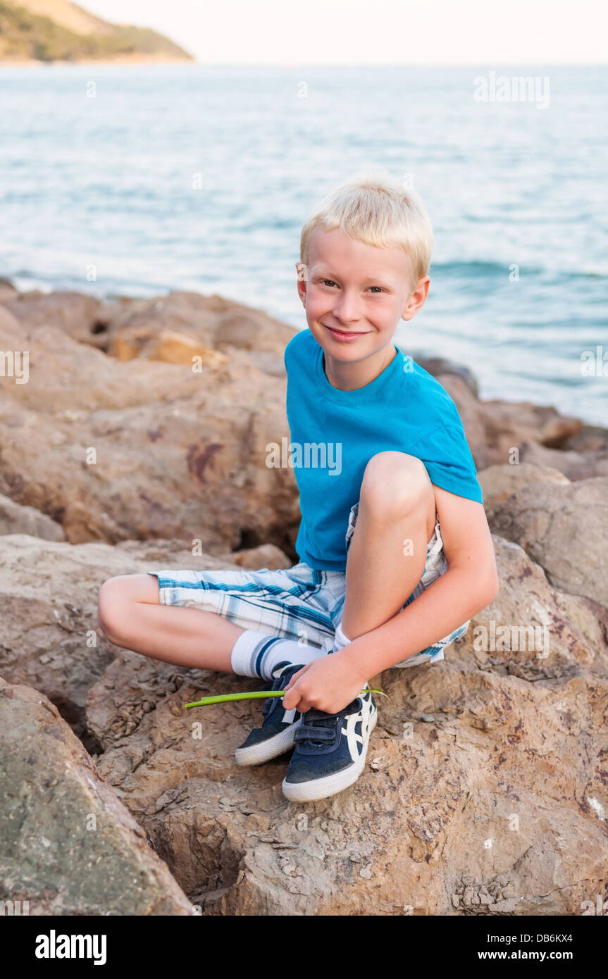 Portrait of young smiling blonde boy, siiting sur une pierre à la côte de la mer Noire Banque D'Images